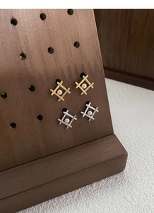 Detailed view of geometric silver pearl earrings in gold and silver on a wooden stand