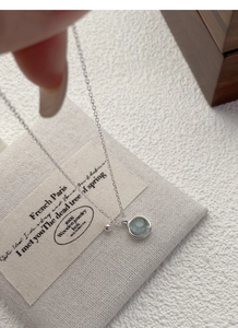 Macro shot of S925 silver necklace with light blue round gemstone on linen background