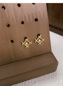Detail of geometric S925 silver pearl stud earrings on a dark wood display stand