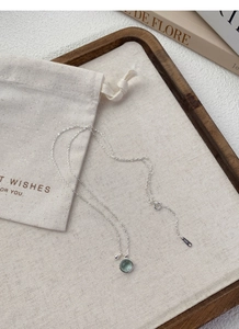 Close-up of S925 silver necklace with green gemstone pendant on beige drawstring pouch