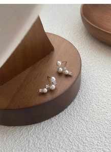 Macro detail of S925 silver pearl stud earrings with zircons on a wooden display stand