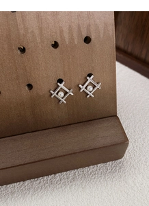 Detail of geometric silver pearl stud earrings displayed on a rustic wooden stand