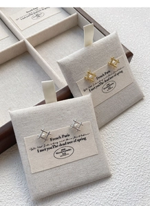 Macro detail of geometric silver and gold pearl stud earrings on textured linen card