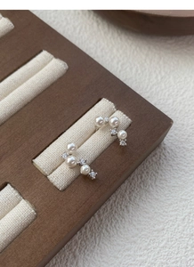 Close-up of S925 silver pearl stud earrings with sparkling diamonds on wood display