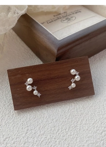 Macro shot of silver pearl and diamond star constellation earrings on wood base