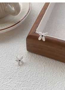 Detail of matte S925 silver gardenia earrings with black stone center on wooden tray