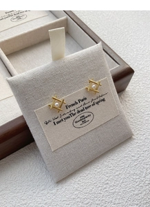 Macro detail of geometric S925 silver pearl stud earrings with gold finish on linen card