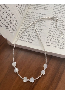 Détail du collier en argent S925 avec cœurs en nacre blanche sur un livre de style rétro