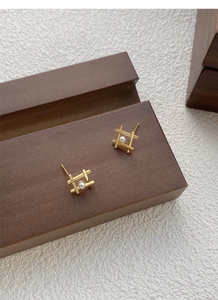 Close-up of geometric gold pearl studs on a dark wooden block with white background
