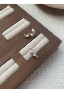 Detailed close-up of S925 silver pearl earrings with sparkling crystals on a wooden stand
