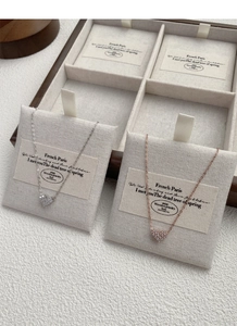 Detail of silver and rose gold heart necklaces with zircon stones in a wooden tray