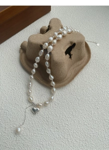 Dettaglio della collana di perle barocche con ciondolo a cuore lucido su sfondo ruvido