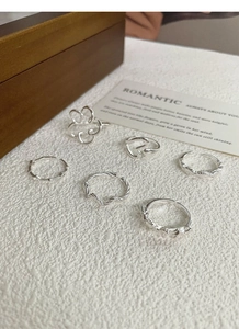 Detail of a 6-piece silver S925 ring set featuring bow and floral motifs on white leather