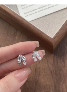 Detailed close-up of S925 sterling silver bow tie stud earrings held by hand