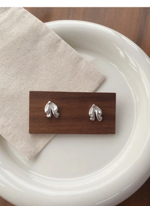 Macro detail of silver bow tie earrings on rustic wood and linen display