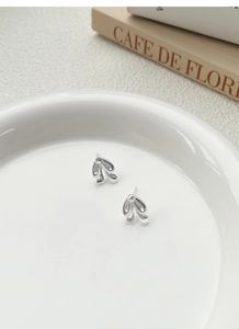 Macro shot of silver bow knot stud earrings with polished metallic leaf layers on a white plate