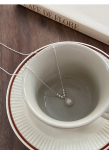 Detailed view of S925 silver pearl necklace placed in a cafe cup with vintage books