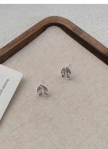 Close-up of polished S925 sterling silver bow knot stud earrings on a linen tray