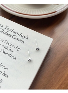 Macro detail of S999 silver flower stud earrings with black gemstone on white magazine