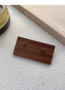 Detailed view of silver clover earrings with black zircon petals on a wooden surface