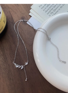 Detail view of S925 silver wheat necklace with marquise zirconia leaf on white ceramic plate
