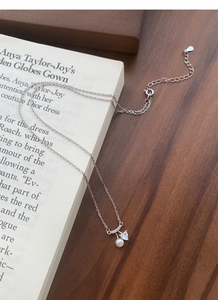 Détail du collier en argent S925 avec perle blanche et zircon cœur sur fond de livre rétro