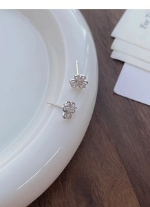 Close-up of S999 silver clover stud earrings with cubic zirconia on white ceramic tray
