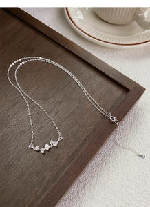 Gros plan détaillé du collier feuille de ginkgo en argent 999 sur plateau en bois
