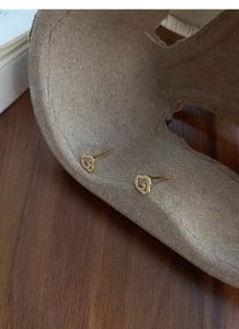 Détail de boucles d'oreilles dorées avec motif nuage évidé sur un plateau chic