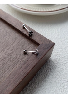 Macro shot of S999 sterling silver clover screw-back studs on dark wood and ceramic texture