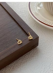 Détail macro de boucles d'oreilles nuage dorées avec logo de luxe sur plateau en bois