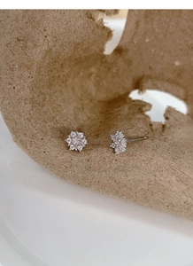 Close-up of S999 silver snowflake earrings with sparkling zircon on textured paper
