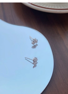 Close-up of S999 silver clover stud earrings with sparkling stones on a mirror surface