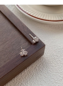 Macro shot of silver clover stud earrings with pavé crystals on a wooden tray