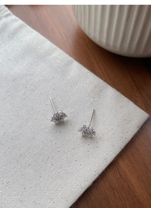 Detailed close-up of sparkling snowflake stud earrings with cubic zirconia on beige fabric