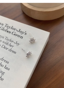 Detail of silver clover earrings with zircons placed on a book page and wood background