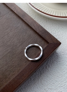 Macro detail of matte silver Mobius ring on a dark wooden tray with minimalist textures