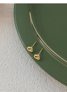 Détail de boucles d'oreilles cœur dorées avec motif G sur surface céramique