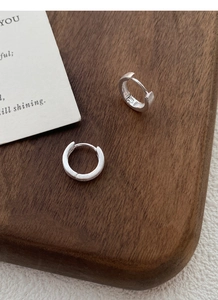 Vue macro des boucles d'oreilles créoles en argent brossé mat sur fond bois foncé