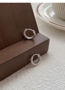 Détail macro de créoles épaisses en argent S999 mat sur un support à bijoux en bois