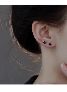 Gros plan de boucles d'oreilles rondes en émail noir en argent S999 portées par un mannequin