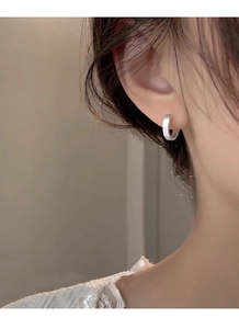Gros plan de boucles d'oreilles créoles larges en argent brossé portées par un modèle
