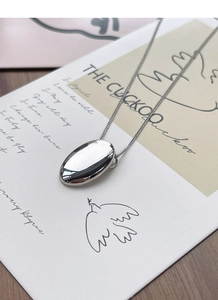 Detailed view of an oval silver pendant on a thin chain over an artistic postcard