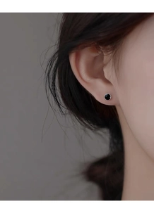 Gros plan d'une boucle d'oreille ronde en argent S999 et émail noir portée à l'oreille