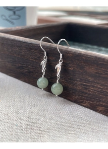 Detail of silver bamboo leaf earrings with green jade beads on a wooden tray