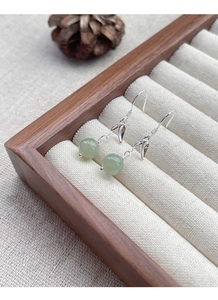 Detail of silver bamboo leaf earrings with green jade beads on a wooden jewelry display box
