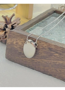Macro view of polished silver oval pendant showing smooth mirror surface and thin O-chain