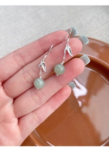 Detail of silver bamboo leaf earrings with round light green jade beads held by hand