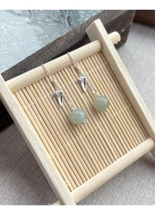 Detailed view of S925 silver bamboo leaf earrings with round green jade on a bamboo stand