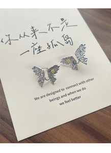 Macro shot of silver butterfly stud earrings with gold flower detail on a card